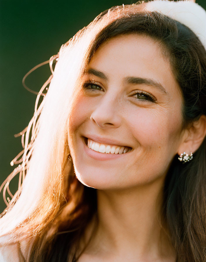 Smiling woman with dark hair in sunlit glow against green background