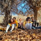 Colorful painting of five people in vintage clothing, laughing under autumn trees.