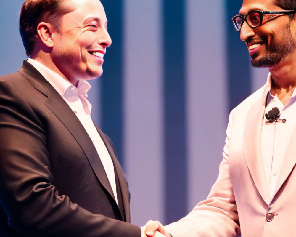 Men in black suit and pink jacket shaking hands on stage, both smiling