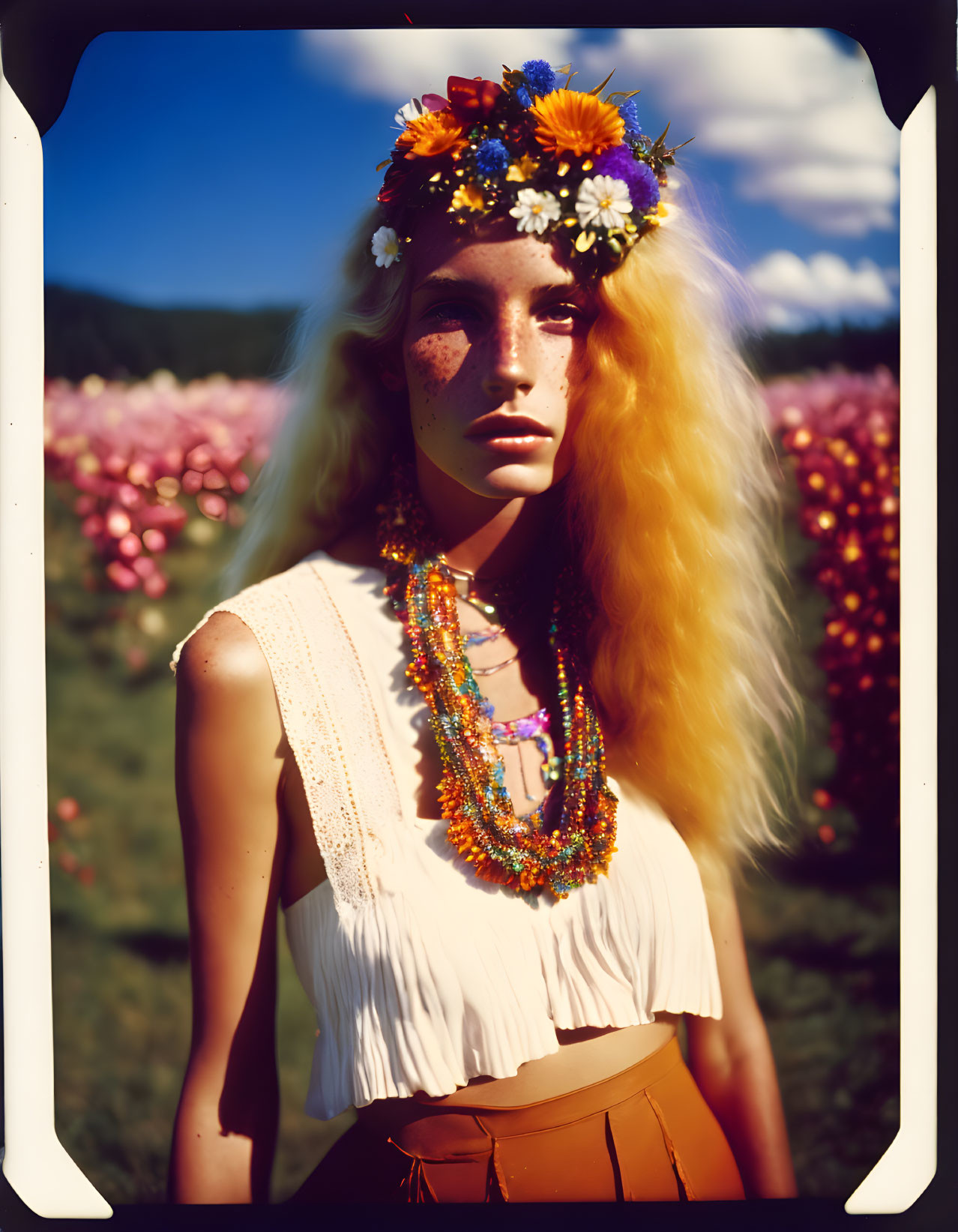 Freckled woman in floral headpiece and necklaces in pink flower field