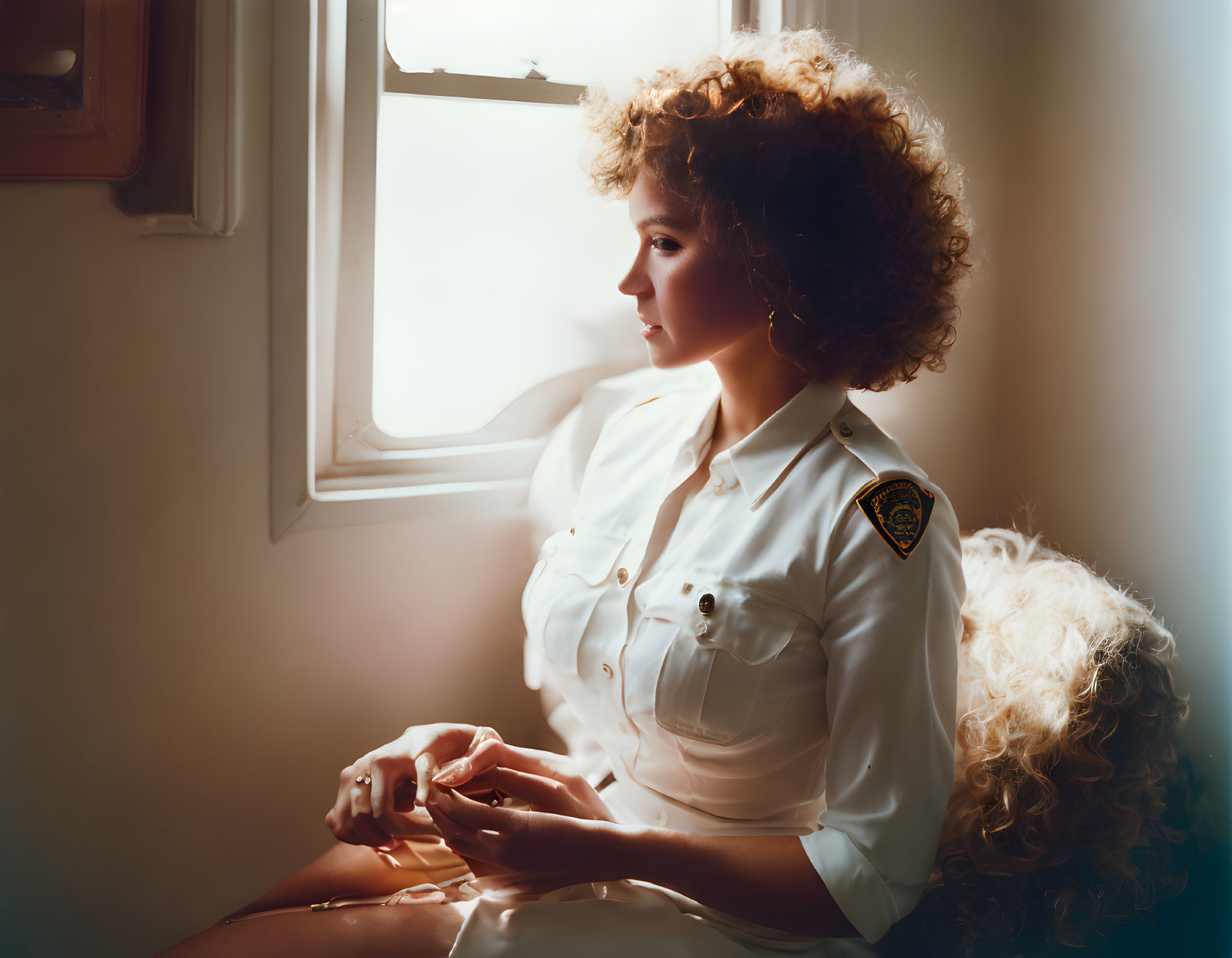 Curly Haired Woman in Uniform Looking out of Sunlit Window