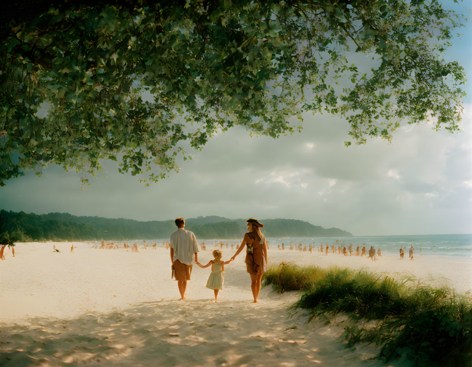 Family of Three Walking on Sandy Beach with Trees and Beachgoers in Distance