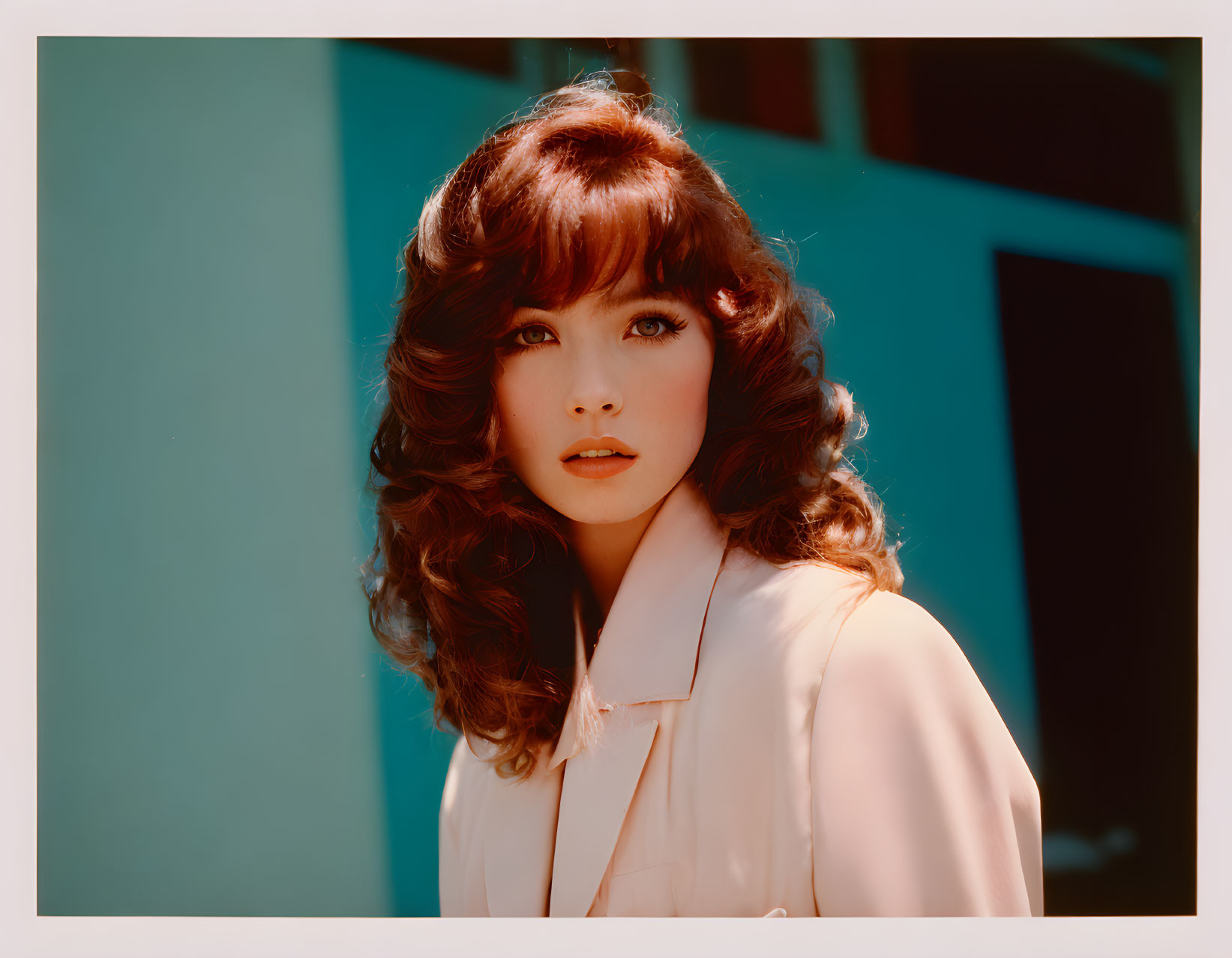 Curly-haired woman in white jacket against teal backdrop