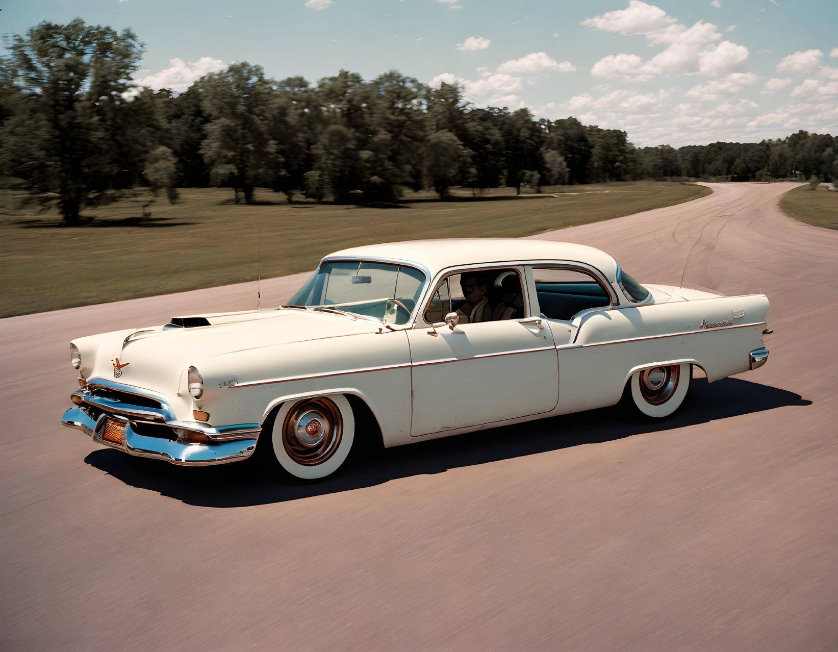 Cream-Colored Vintage Car Driving with Person Inside, Trees and Blue Sky in Background