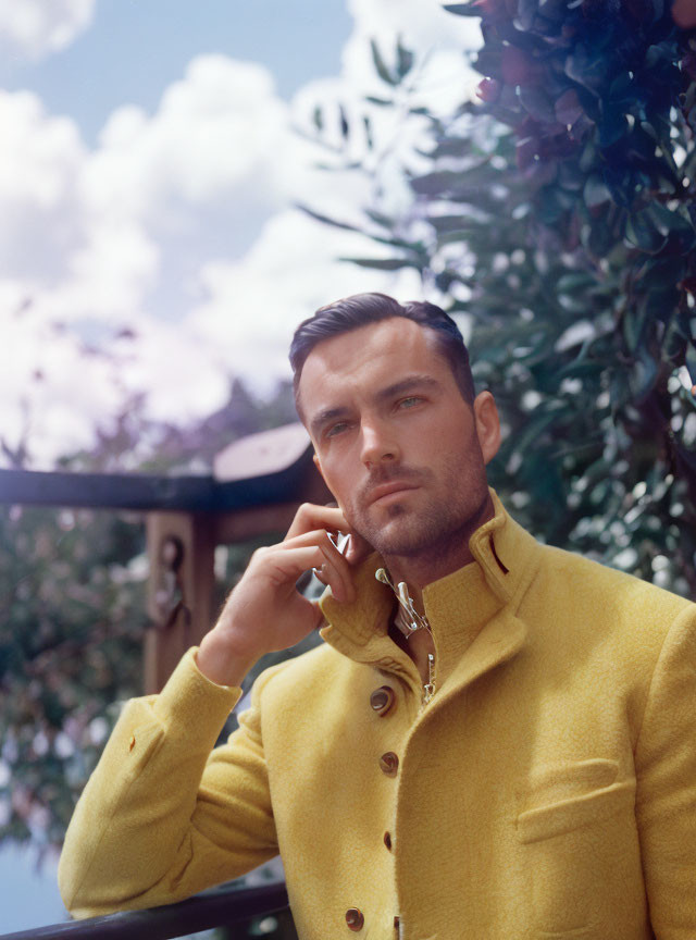 Man with Short Dark Hair in Yellow Jacket Against Blurred Plant Background