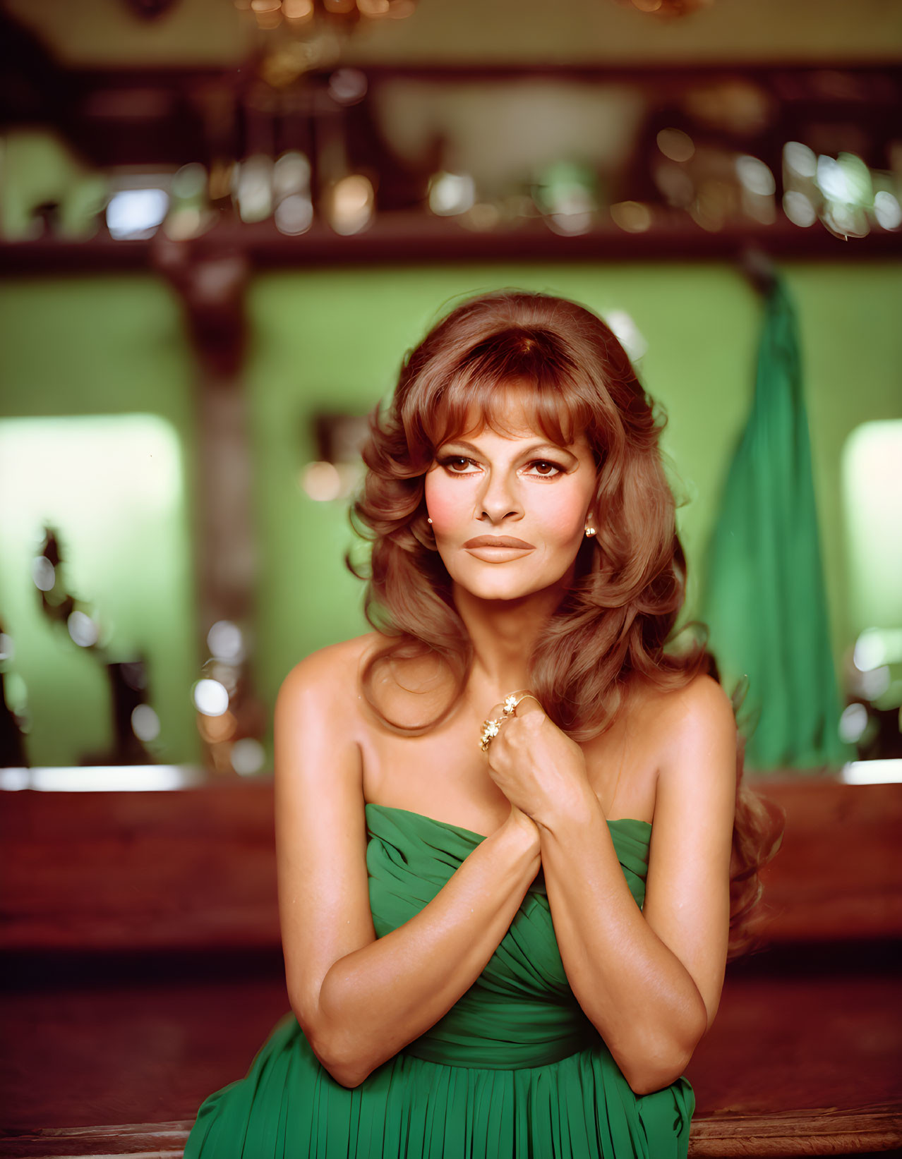 Woman with voluminous hair in green strapless dress at bar, hands clasped, wearing gold ring