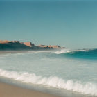 Tranquil beach scene with cresting wave, misty sea spray, clear skies, and cliffs