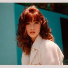 Curly-haired woman in white jacket against teal backdrop