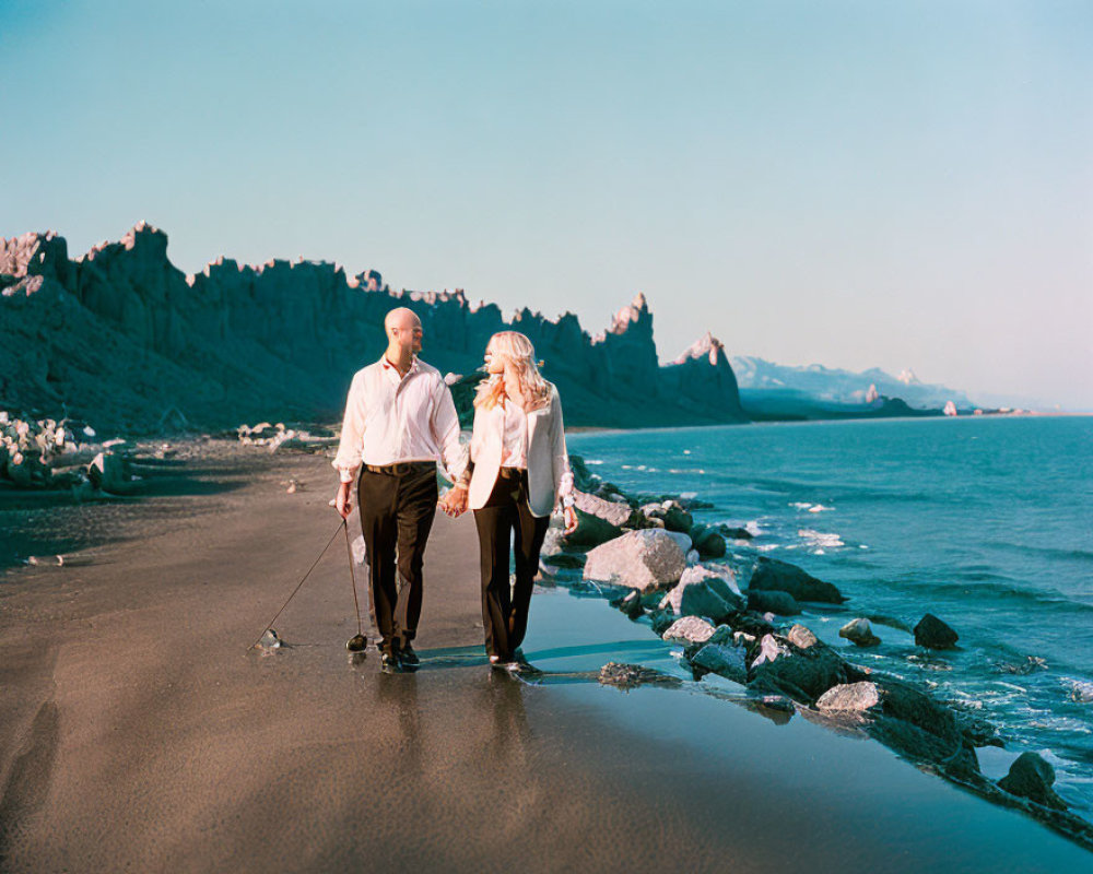 Couple walking hand-in-hand on serene beach with cliffs and calm sea