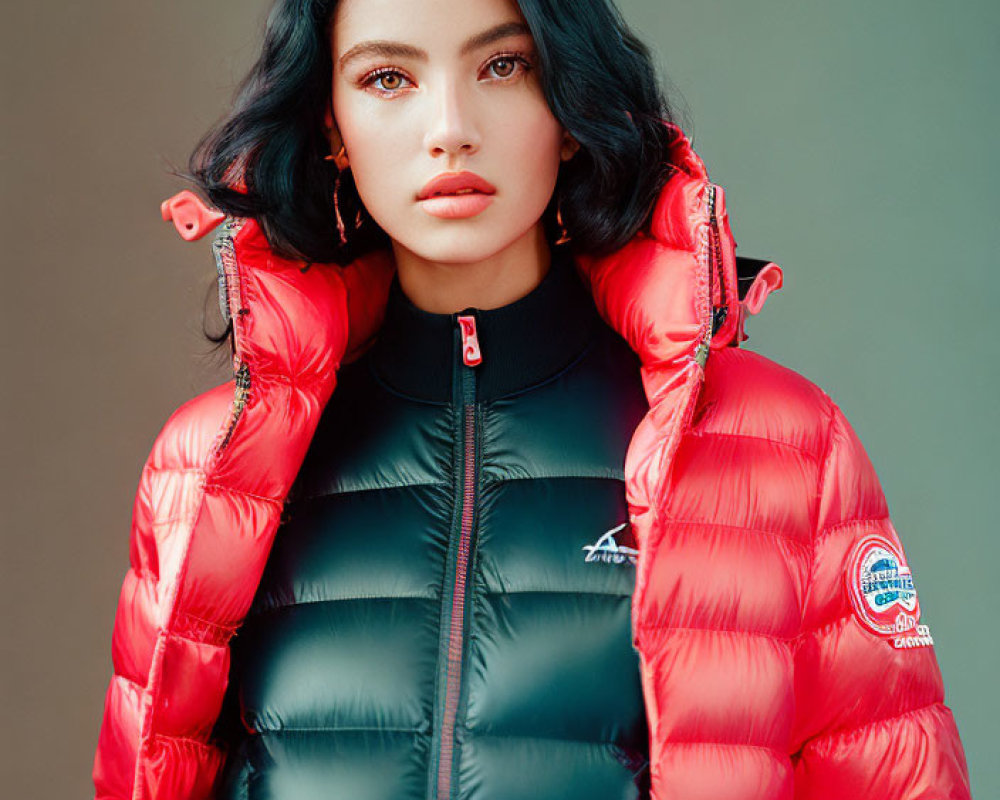 Dark-haired woman in red and black puffer jacket on neutral backdrop