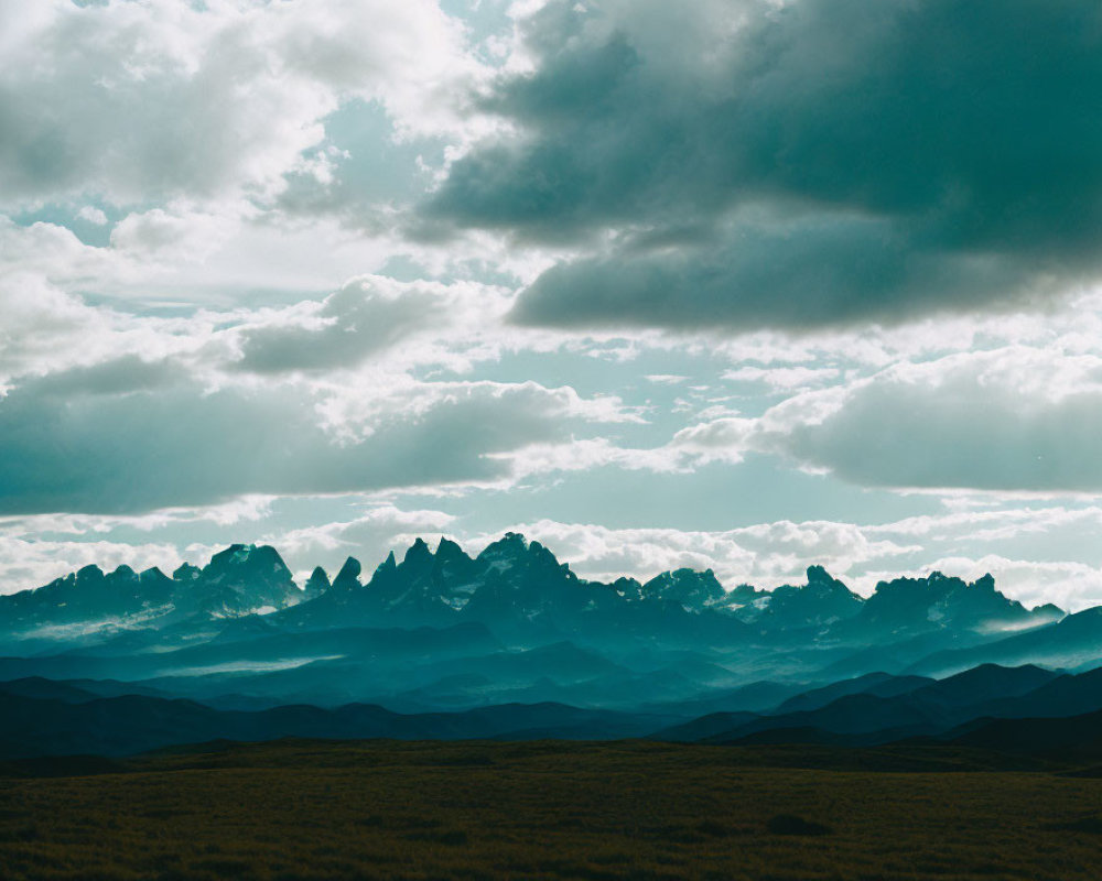 Majestic mountain peaks under dramatic cloudy sky with sunrays.