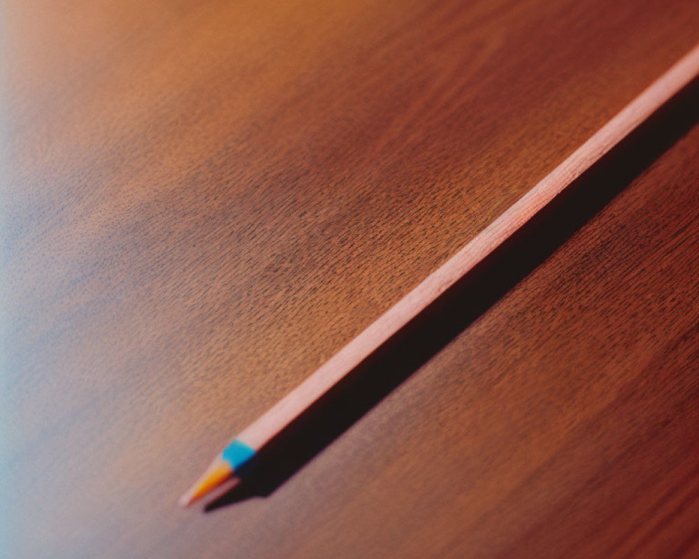 Wooden pencil with blue tip on smooth brown surface, diagonal position.