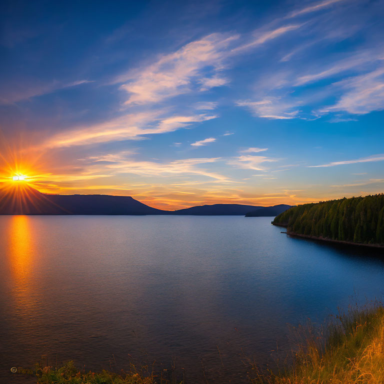 Tranquil lake sunset with sun rays, forested coastline, and gradient sky