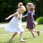 Young girls holding hands in sunny meadow with green trees and pink flowers