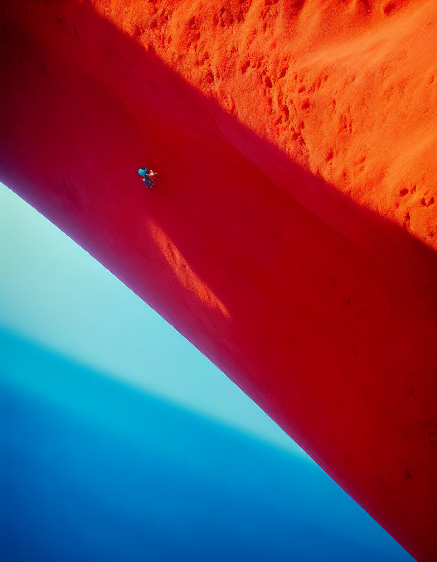 Climber ascending steep red rock face against blue sky