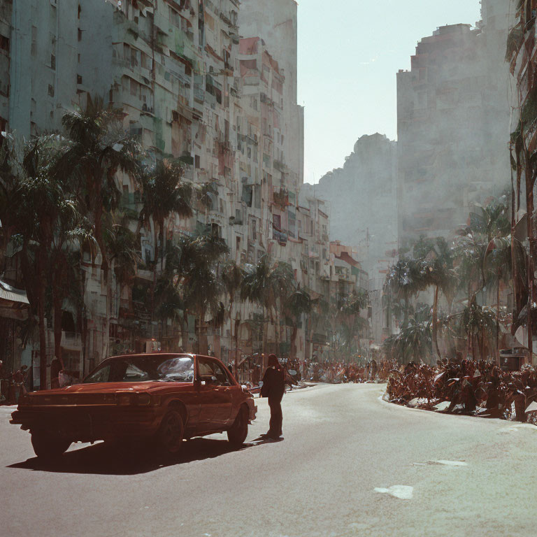 Vintage Red Car Driving on Sunlit City Street with High-Rise Buildings and Parked Motorcycles