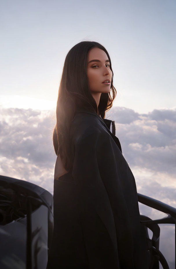 Woman in black outfit gazing over shoulder at twilight clouds.