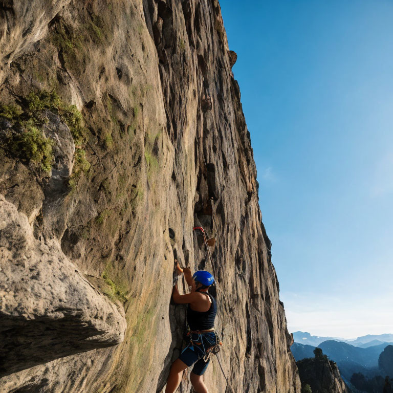 Rock climber in blue helmet ascending steep cliff against mountain backdrop