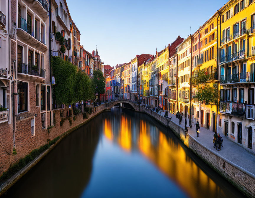 Scenic canal with colorful buildings, bridge, and reflections at dusk