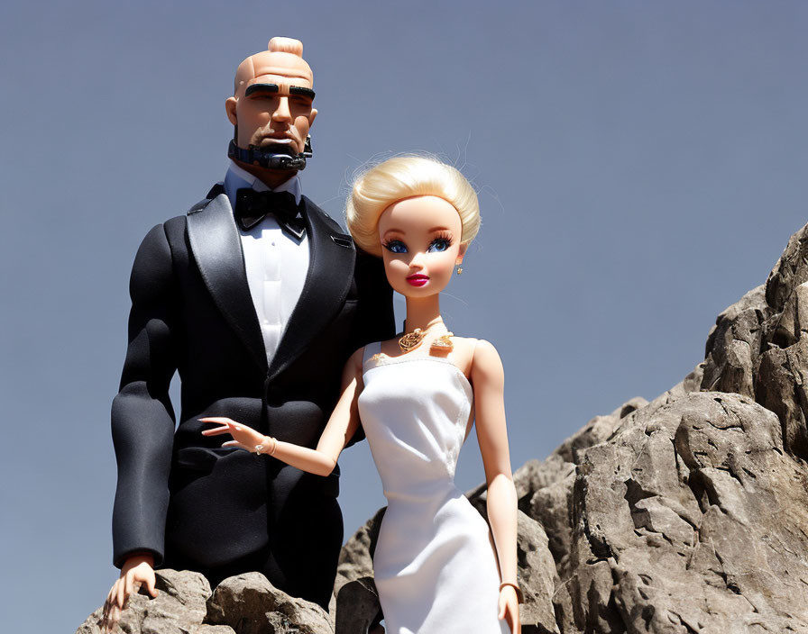 Male and female dolls in formal attire against rock and sky backdrop