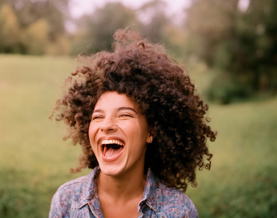 Curly-haired woman laughing outdoors with green backdrop