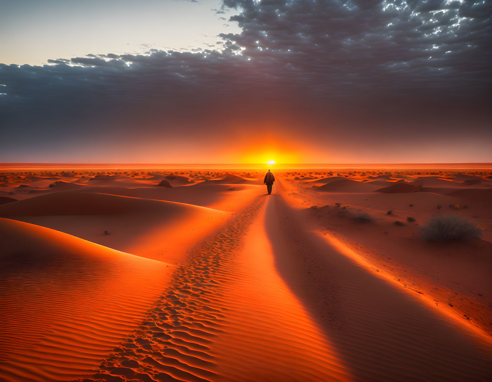 Person standing on desert dune at dramatic sunset.