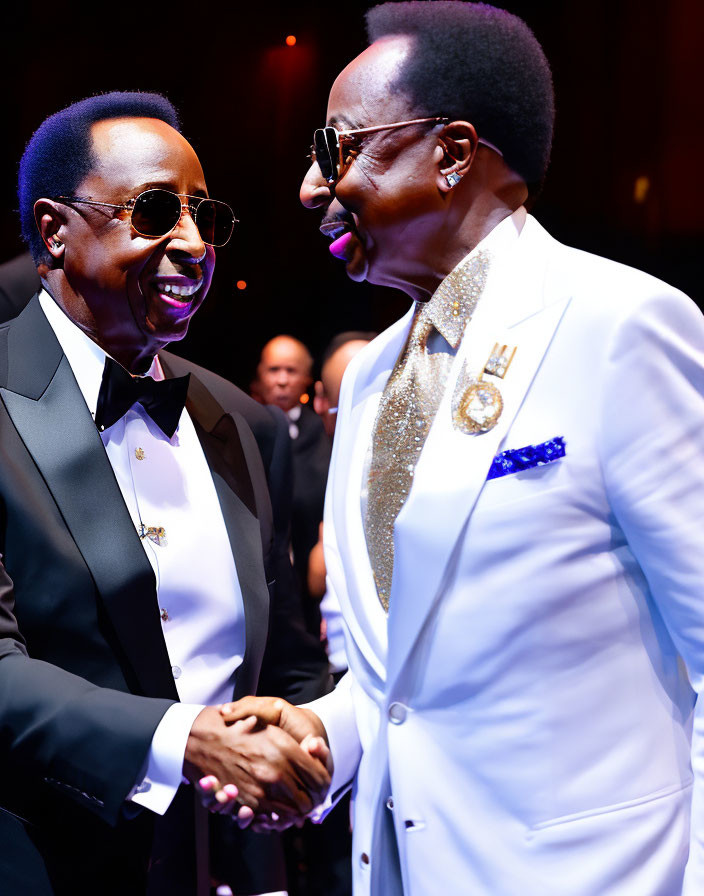 Two men in elegant suits shaking hands on stage with warm lighting.