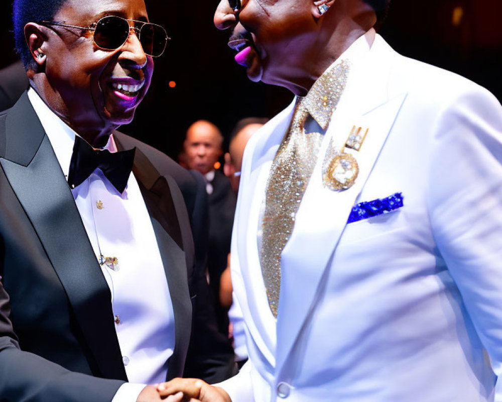 Two men in elegant suits shaking hands on stage with warm lighting.