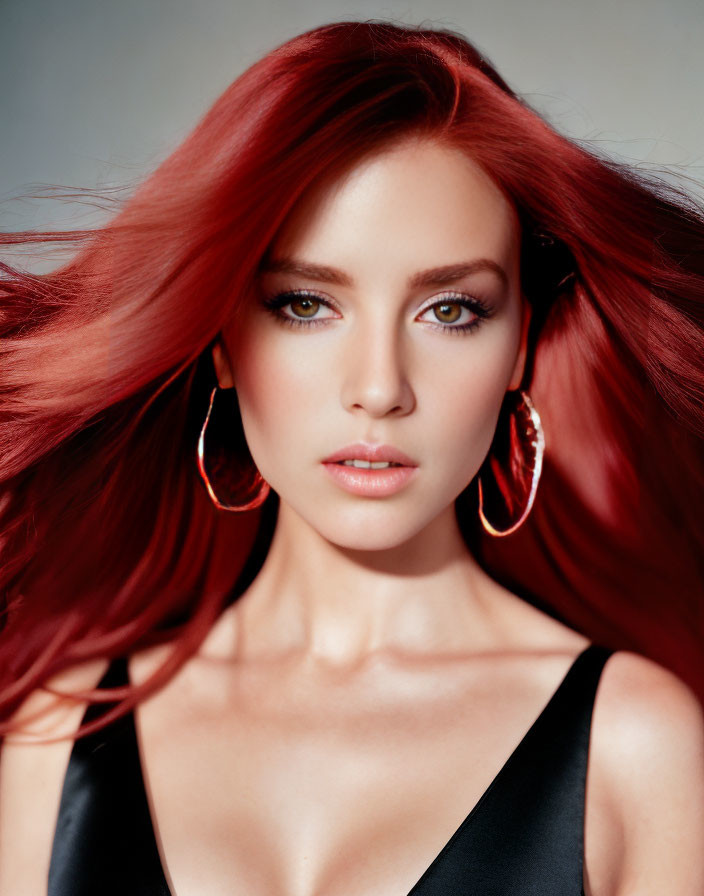 Portrait of woman with red hair and green eyes in black top and gold earrings