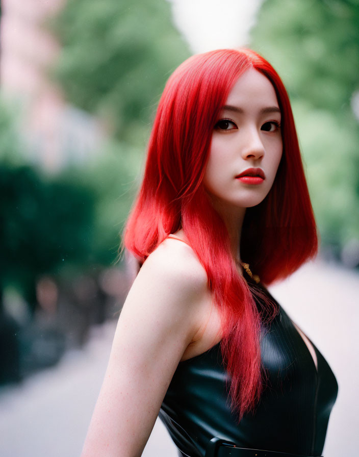 Red-haired woman in black outfit outdoors with blurred trees.