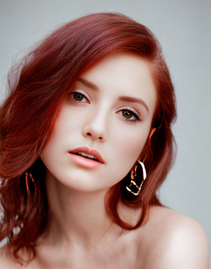 Red-haired woman with hoop earrings in subtle makeup on neutral background