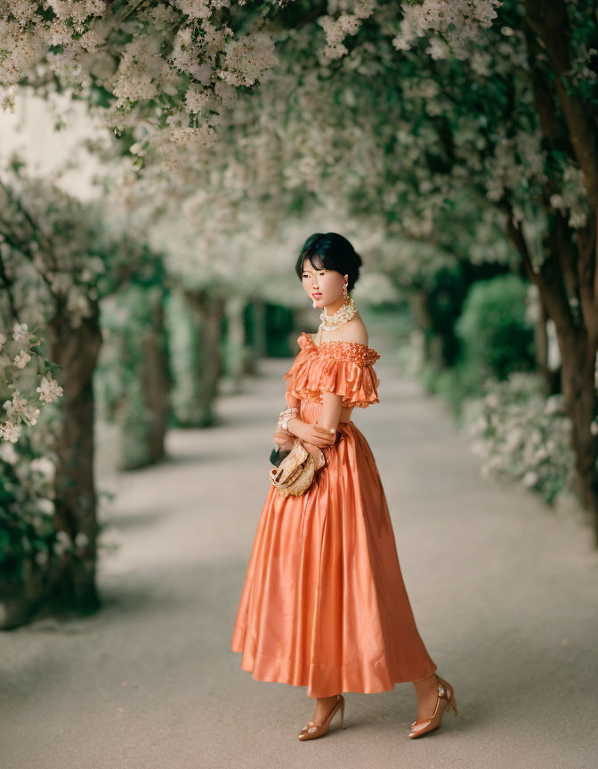 Elegant Woman in Orange Dress Among Blooming Trees