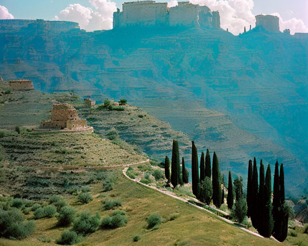 Green hillside with cypress trees & ancient fortress ruins under blue sky