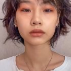 Curly-haired woman with artistic makeup and pendant necklace in white top