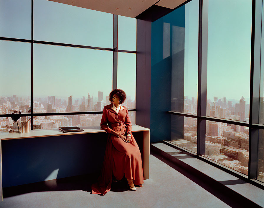 Pensive woman in terracotta dress by window with cityscape view