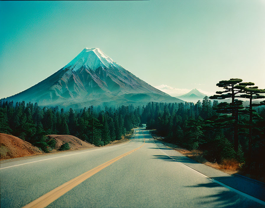 Snow-capped mountain and open road scene with evergreen trees