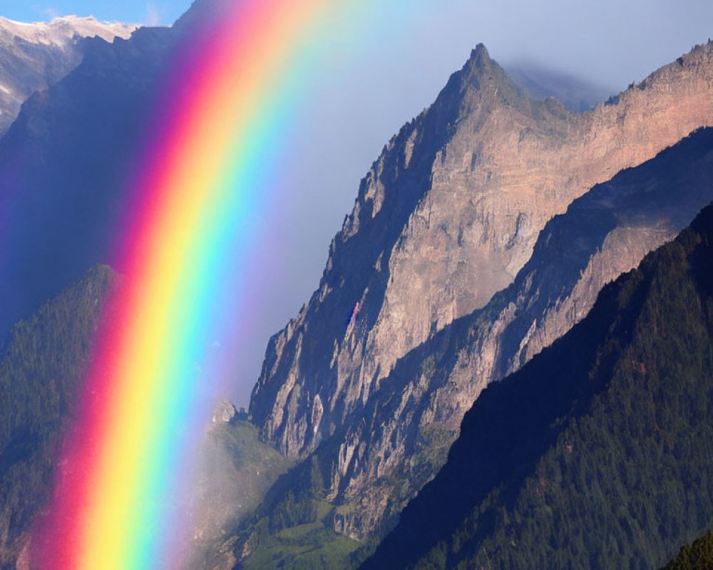 Colorful rainbow over cloudy mountain in sunlight