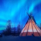 Northern Lights illuminate snowy landscape with teepee under starry sky