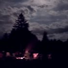 Person and child admiring moon by shore at night with glowing tent and distant boat