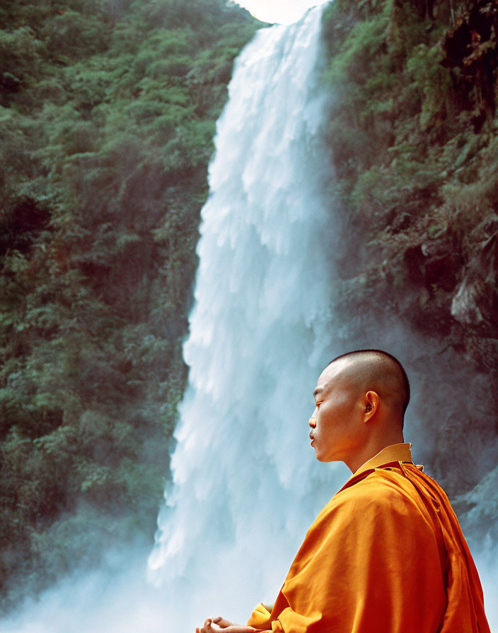 Orange-robed monk meditating by lush waterfall and cliffs