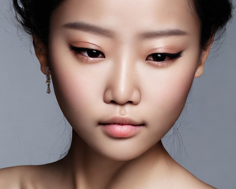 Close-up portrait of woman with subtle makeup and elegant earring on grey background