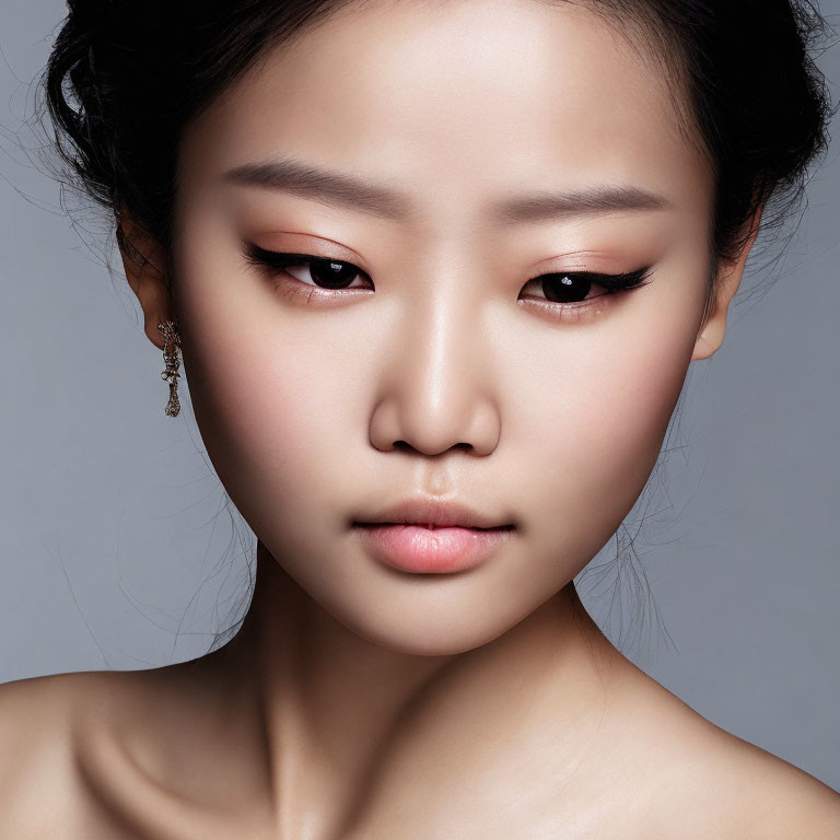 Close-up portrait of woman with subtle makeup and elegant earring on grey background