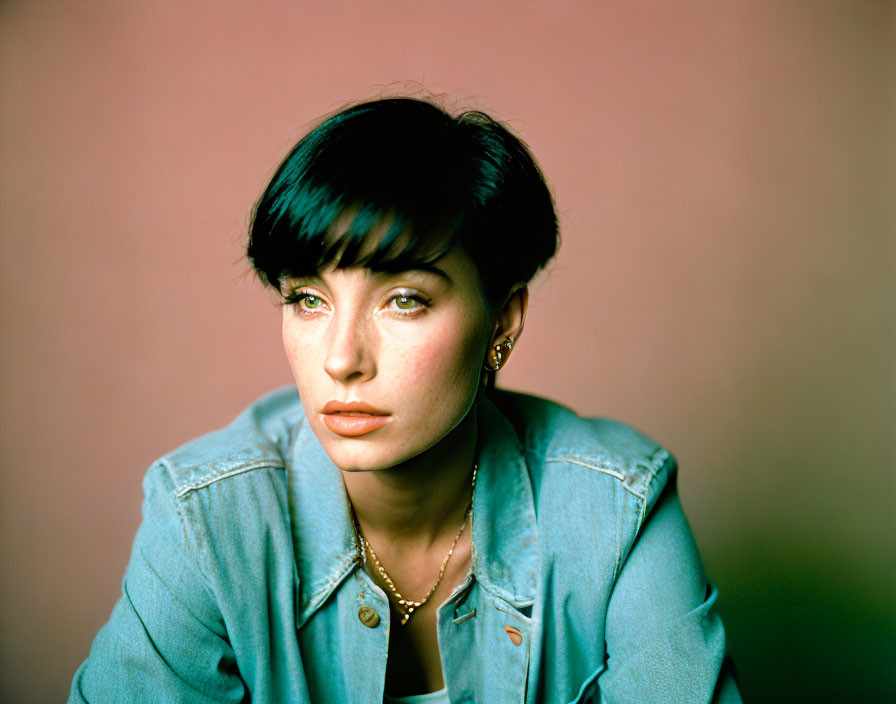 Dark-Haired Woman in Denim Jacket and Necklace on Pink Background