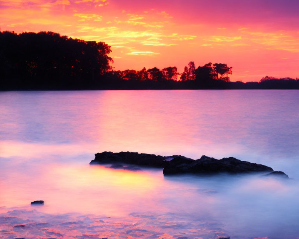 Colorful sunset over lake with tree silhouettes and rocks.