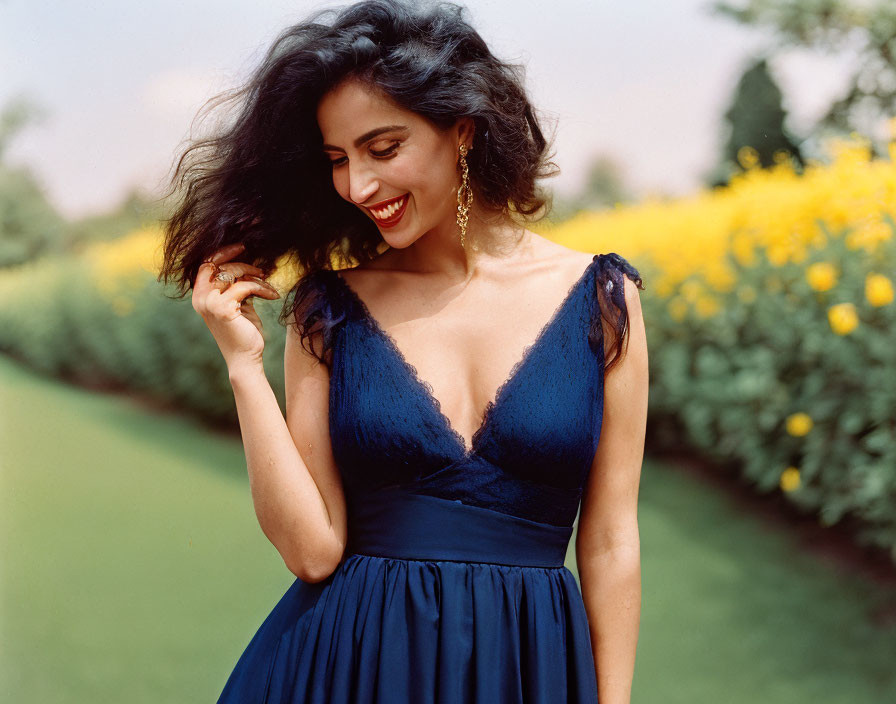 Smiling woman in blue dress surrounded by lush greenery and yellow flowers