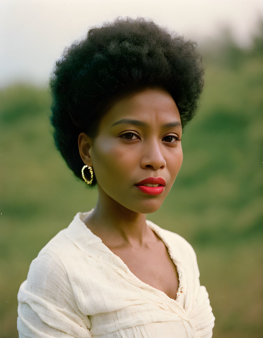 Woman with natural afro and red lipstick in white top and hoop earrings on green background.