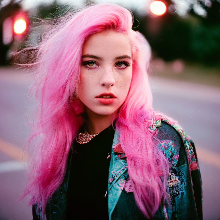 Young woman with pink hair in denim jacket under dusky sky