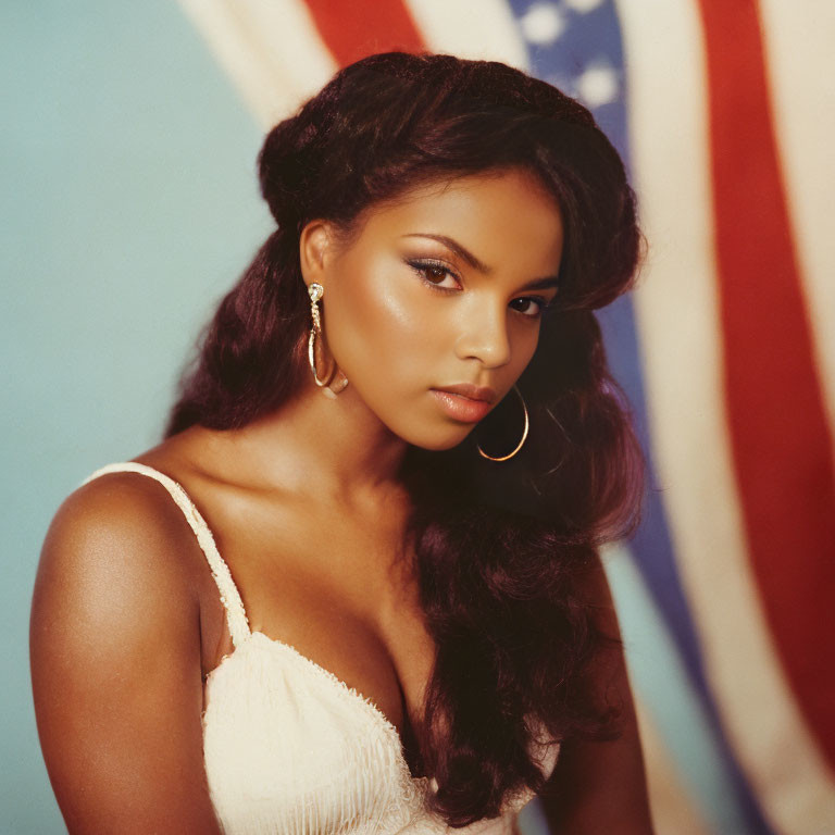 Woman with wavy hair, hoop earrings, white top in front of American flag