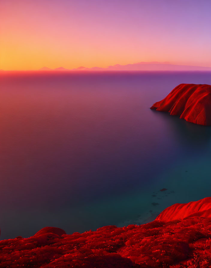 Colorful sunset over sea with mountain silhouettes and red hill.