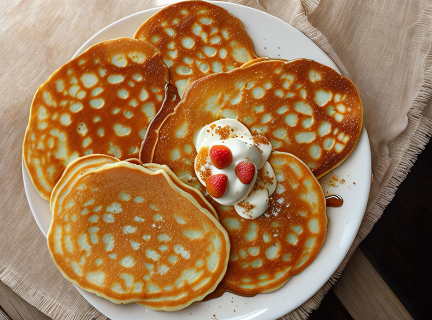 Golden-brown pancakes with syrup, whipped cream, and strawberries on white plate